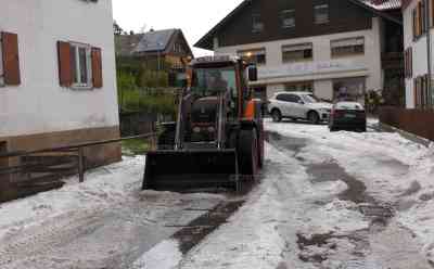 Schweres Hagelunwetter - Radlader gegen Hagelmassen: Forggensee gleicht einer Winterlandschaft, Radfahrerin schiebt Rad in 10 cm hohem Hagel, Hagelberge vor Grundstücke und Einfahrten: Idyllischer Forggensee schneeweiß, auch Bundesstraße 50 cm hoch vom Hagel bedeckt, Superzelle ursächlich dafür